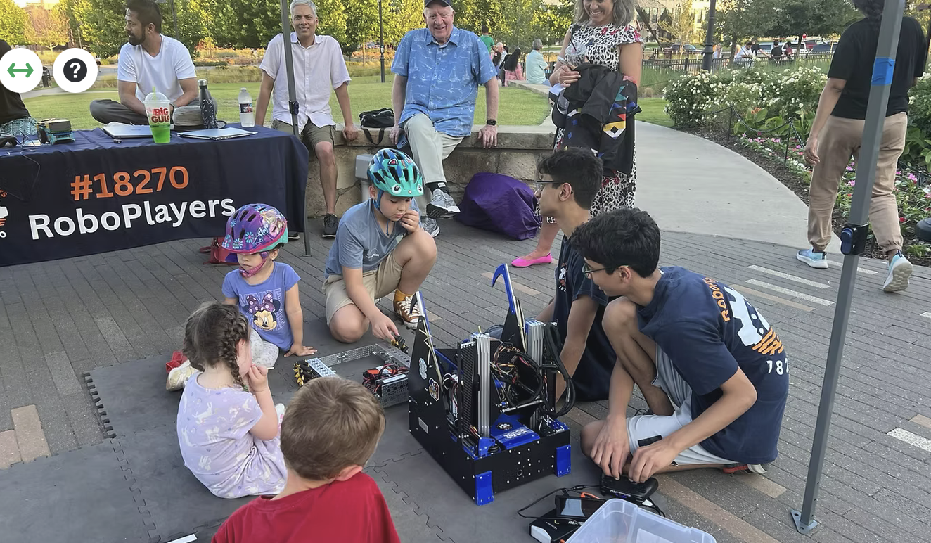 RoboPlayers team members showing their robot to younger kids gathered around at a community event