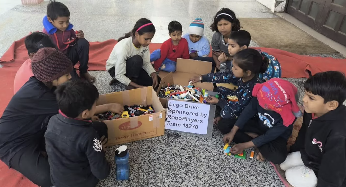 Children in India gathered around boxes of donated LEGO bricks labeled Lego Drive Sponsored by RoboPlayers Team 18270